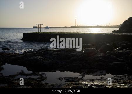 sun setting over swimming platform and rocky volcanic shoreline playa blanca lanzarote, canary islands, spain Stock Photo