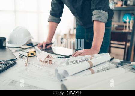 Mini model house on blueprint plan while architector standing and working background. House Architect design and engineer concept. Stock Photo