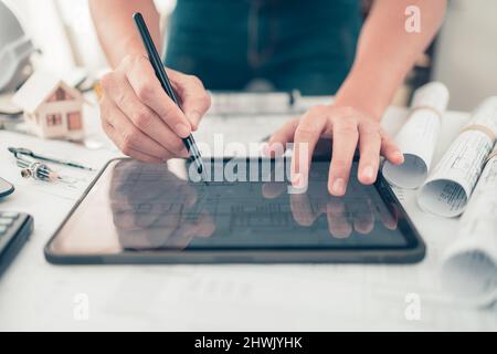 Architect engineer use tablet read and check drawing design working on bueprint. House planning design and construction concept. Stock Photo