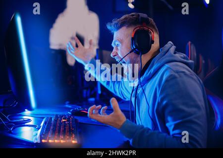 Streamer young man angry professional gamer playing online losing game computer with headphones, neon color. Stock Photo