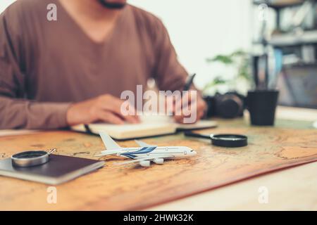 model airplane on world map and book, magnifying glass, compass and camera on map and man writing . Travel , Adventure and Discovery concept. Stock Photo