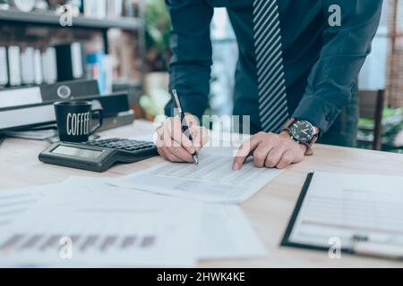 Accountant writing, checking and working on company data, document, report and calculator to calculate  on desk office. Accounting business concept. Stock Photo