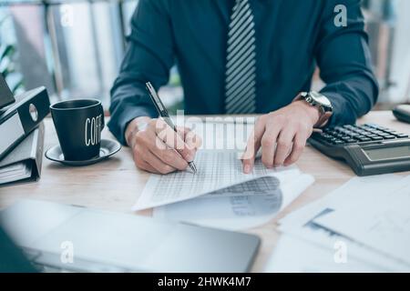 Accountant writing, checking and working on company data, document, report and calculator to calculate  on desk office. Accounting business concept. Stock Photo