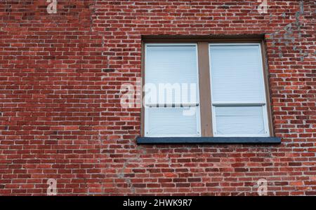 Window in Brick Wall. Window with closed blinds in a urban red bricks clinker house. Street photo, nobody, selective focus, copy space for text Stock Photo