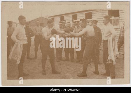 Army boxing match in a camp of the Royal Engineers, early 20th century. Two soldiers, stripped to the waist & wearing boxing gloves, are sparring. They are watched by their seconds, carrying towels, and a small group of soldiers. Barracks huts can be seen in the background of the photograph Stock Photo