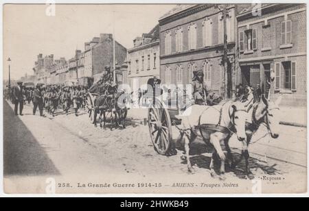 'La Grande Guerre 1914-15 - Amiens - Troupes Noires': First World War French postcard of North African soldiers marching through the city of Amiens (on the Somme river). Two horse drawn carts are leading the column of troops and some bystanders are watching the column march by Stock Photo