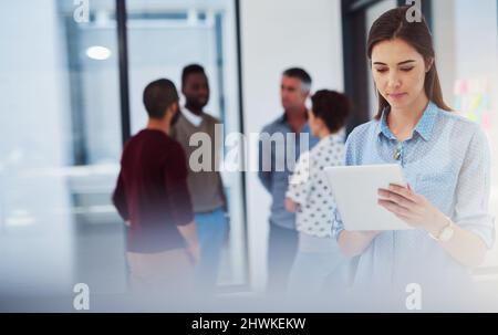 Checking a few emails. Cropped shot of a young businesswoman working in the office with her colleagues in the background. Stock Photo