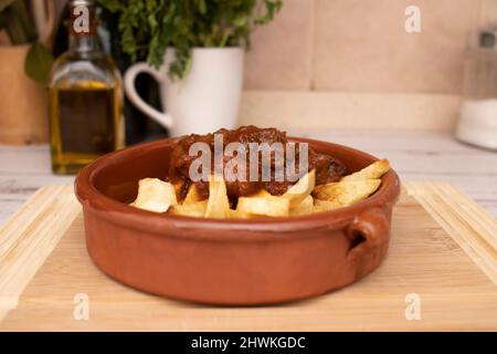 A rustic clay plate with goulash and potatoes, placed on a wooden board. Traditional foods concept. Stock Photo