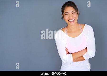 Motivate yourself or no one will. Cropped shot of a sporty young woman standing with her arms folded against a grey background. Stock Photo