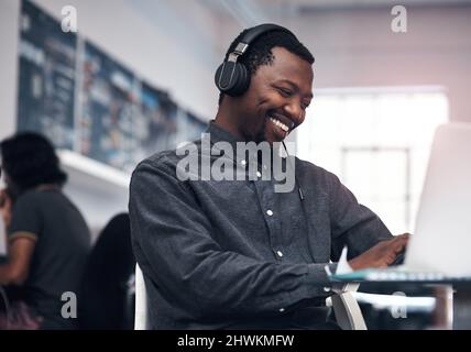 Music makes work so much enjoyable. Cropped shot of a handsome young businessman using a laptop while wearing headphones in a modern office. Stock Photo
