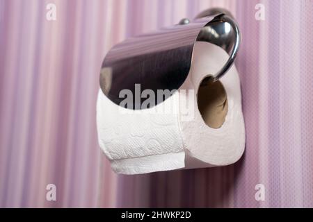 Close-up of a white roll of soft toilet paper hanging neatly on a chrome holder on the lilac toilet wall Stock Photo