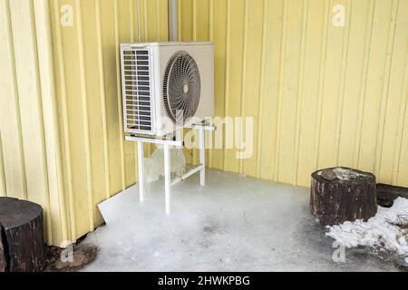 Air conditioner machine outdoors on rack on domestic home house yellow wall. Lot of ice under it in cold winter day. Stock Photo