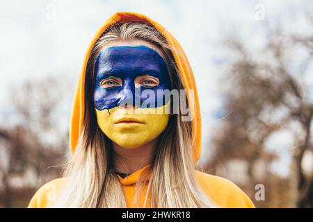 Outdoor portrait of young girl with blue and yellow ukrainian flag on her face. Stop war in Ukraine. Russia stop war. Stock Photo