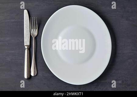 Oval white plate on a dark concrete background with cutlery Stock Photo