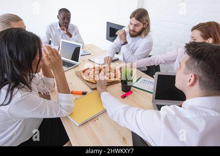 Diverse business team people workers eating pizza together at workplace, friendly multi-ethnic colleagues group talking enjoying having fun and corpor Stock Photo