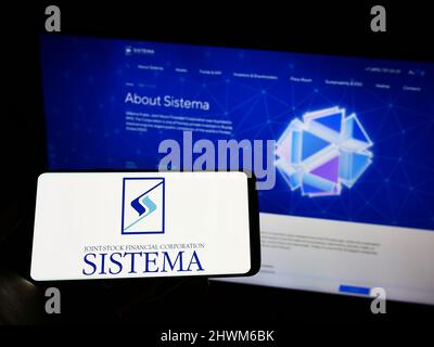 Person holding cellphone with logo of Russian conglomerate AFK Sistema PAO on screen in front of company webpage. Focus on phone display. Stock Photo