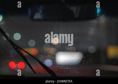 Windshield wipers working in heavy rain in the city night. Night view of windshield wipers cleaning the water accumulated on windscreen. Stock Photo