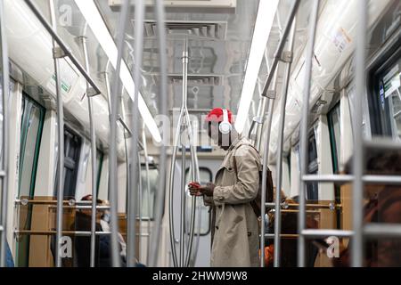 Black hipster man wear wireless headphones, listening to the music, using smartphone in subway train Stock Photo