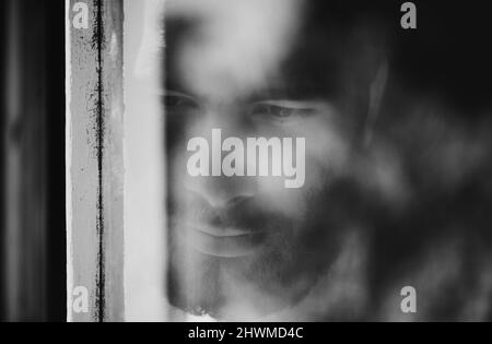 Blurred viewpoint. Closeup of a thoughtful young man seen through a window. Stock Photo