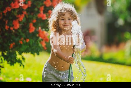 American child playing with garden hose in backyard. Funny excited kid having fun with spray of water on yard nature background. Summer kids outdoors Stock Photo