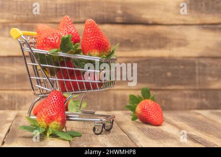 Fresh strawberries in a shopping cart on a wooden background. Lots of ripe sweet strawberries in a basket. Close-up. Side view and space for text Stock Photo