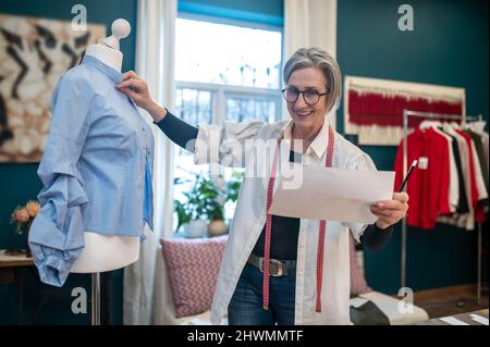 Woman with sketch standing touching blouse on dummy Stock Photo
