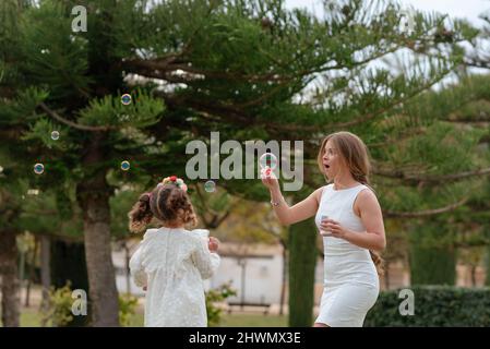 Mother and daughter blow soap bubbles outdoors. Stock Photo