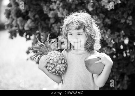 Child boy holding pineapple and coconut smiling with happy face in yard. Summer fruits. Stock Photo