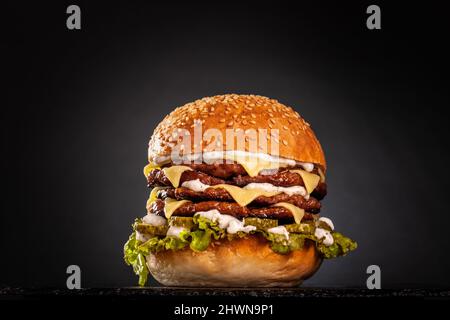 Quadruple burger with cheese cucumber and lettuce. Isolated on black background. Stock Photo