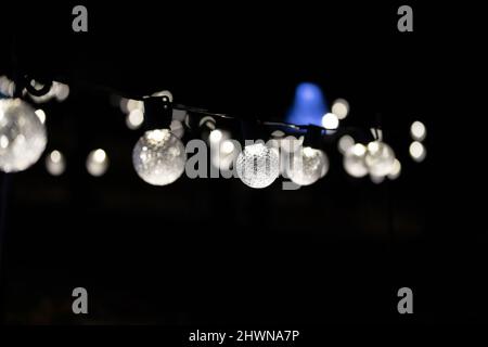 string of round decorative light bulbs on a black background with a blue light ray in the background, dissipate into bokeh effect with copy space Stock Photo