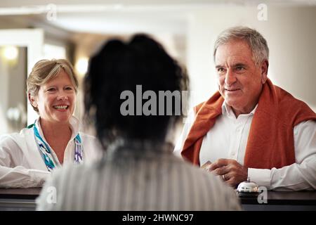 Welcome. We hope you enjoy your stay. Cropped shot of a senior couple checking in at the hotel. Stock Photo