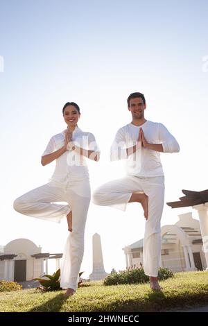 Demonstrating a perfect tree pose. Full length shot of a young couple doing yoga outdoors. Stock Photo