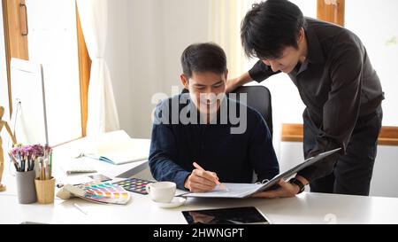 Two young male graphic designers co-working on a new project, discussing the plan for their design in the office. Creative workspace. Stock Photo