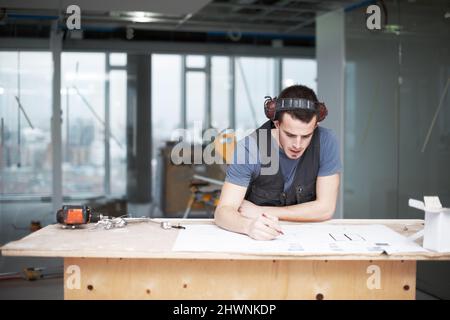Working to create a precise design. Young architect working on his plans while at a construction site. Stock Photo