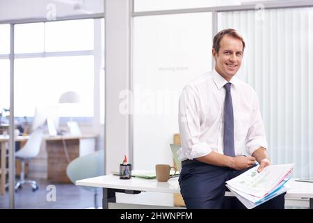 Happy friday finance review. Portrait of a handsome young businessman reading through documents in his office. Stock Photo