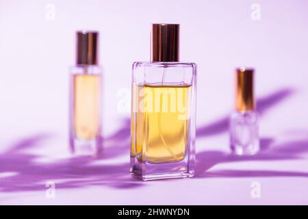 Three glass transparent rectangular bottles of golden perfume on lilac background with sunlight and shadows of leaves. Minimal style perfumery templat Stock Photo