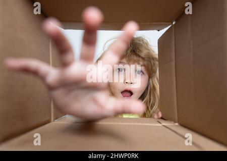 Child boy opening a carton box and looking inside, take by hand gift. Unpacking concept, surprise unboxing. Parcels and delivery. Stock Photo