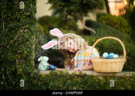 Cute child bunny wear rabbit ears in garden, Happy Easter day. Bunny boy with easters basket, funny outdoor portrait. Hunting eggs and spring holidays Stock Photo