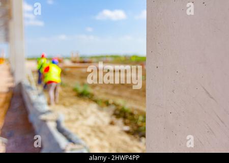 Clouse-up view on beam, pilar of unfinished concrete edifice. People are working in background with safety vests and helmets. Stock Photo