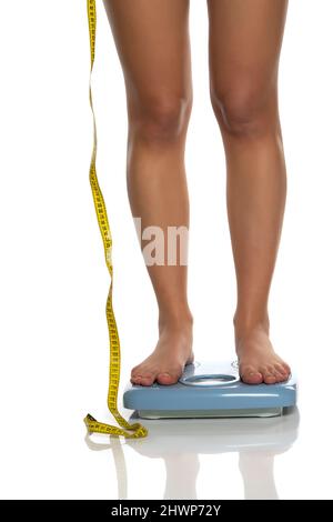 female legs on scales and measuring tape next to them on a white background Stock Photo