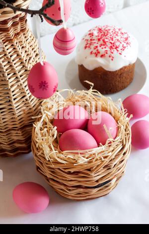 Easter composition with pink colored eggs in wicker basket and Easter cake on white background Stock Photo