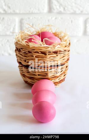 Minimalistic Easter composition with wicker basket and pink colored eggs on white background Stock Photo