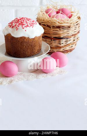 Minimalistic Easter composition with wicker basket with pink colored eggs and Easter cake on white background. Copy space Stock Photo
