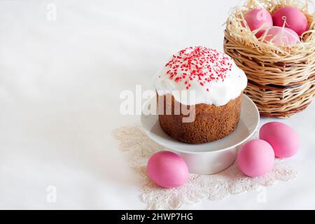 Minimalistic Easter composition with wicker basket with pink colored eggs and Easter cake on white background. Copy space Stock Photo