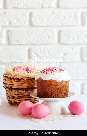 Minimalistic Easter composition with wicker basket with pink colored eggs and Easter cake on white background. Copy space Stock Photo