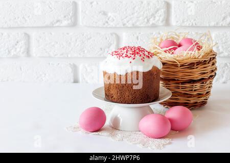 Minimalistic Easter composition with wicker basket with pink colored eggs and Easter cake on white background. Copy space Stock Photo