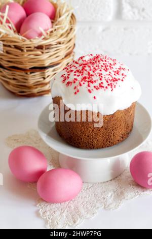 Minimalistic Easter composition with wicker basket with pink colored eggs and Easter cake on white background Stock Photo