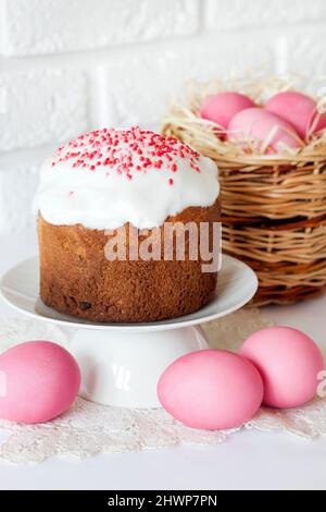 Minimalistic Easter composition with wicker basket with pink colored eggs and Easter cake on white background Stock Photo