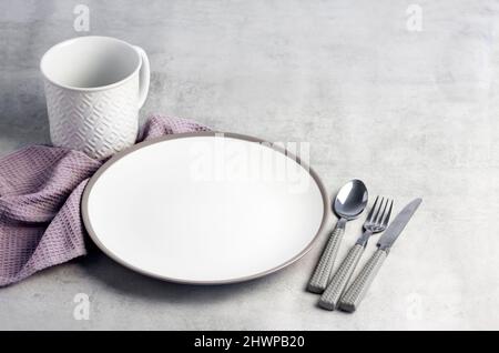 Table setting. White plate, mug, cutlery and napkin on light gray background. Stock Photo