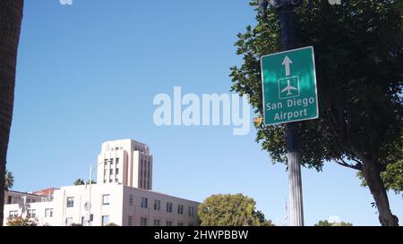 Airport green road sign with direction arrow and plane icon, San Diego city street, California USA. Tourist destination, traffic signage. Local and international travel concept. Civic center building. Stock Photo
